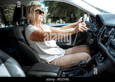 Senior business woman driving a car, view from the inside of a vehicle. Concept of an active people during retirement age Stock Photo