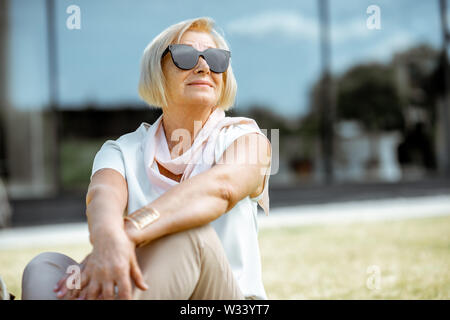 Lifestyle portrait of an elegant senior business woman dressed in white shirt sitting outdoors in the city. Concept of an active people during retirem Stock Photo