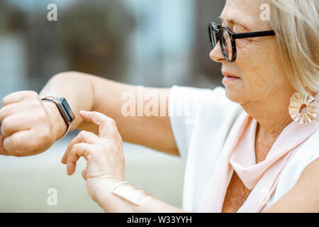 Senior woman using smart watch outdoors. Concept of using modern technologies by elderly people Stock Photo