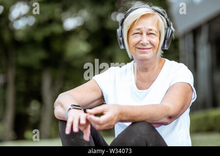 Portrait of a happy senior woman in sports clothes with headphones outdoors. Concept of a healthy lifestyle on retirement Stock Photo