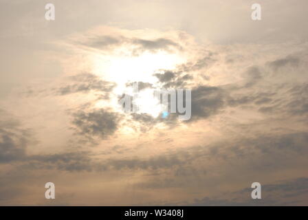 Hazy diffuse sun shining behind  grey clouds in a fuzzy  abstract sky Stock Photo