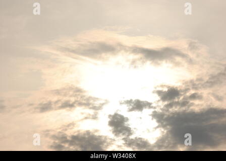 Hazy diffuse sun shining behind  grey clouds in a fuzzy  abstract sky Stock Photo