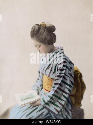 [ 1890s Japan - Japanese Woman in Kimono ] —   Young Japanese woman in kimono and traditional hairdo reading a book.  19th century vintage albumen photograph. Stock Photo