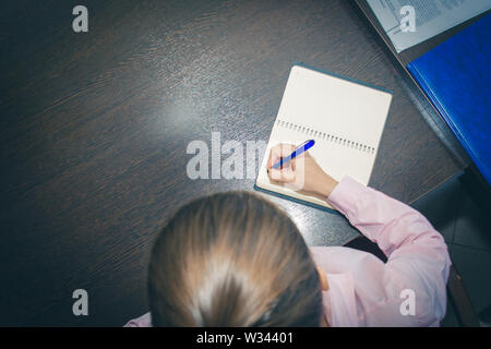 young woman hands holding open notebook pages on a dark table, top view. shopping list. the plan of action for the Notepad Stock Photo