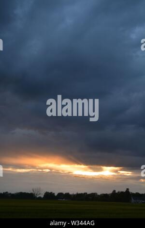 Sunset with the sun glow along the bottom of a large cloud bank that fills the sky Stock Photo
