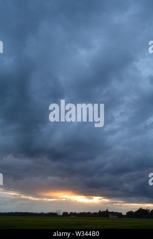 Sunset with the sun glow along the bottom of a large cloud bank that fills the sky Stock Photo