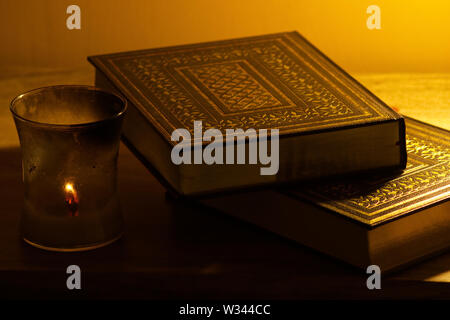 Copies of old religious books and texts next to a lit candle against a gold background Stock Photo