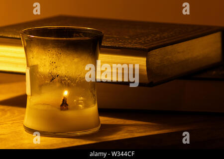 Copies of old religious books and texts next to a lit candle against a gold background Stock Photo