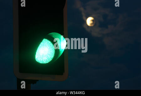 A green traffic light with a full moon in the background