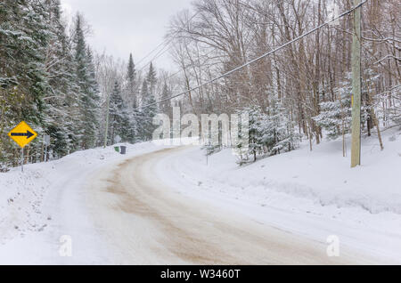 Winding mountain road through a forest covered in snow during a snowstorm Stock Photo