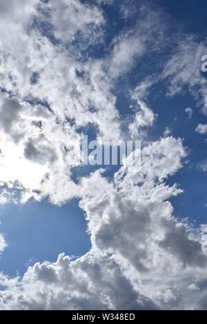 White fluffy clouds against a blue sky with the sun breaking  through the edge. Nice background pattern. Stock Photo