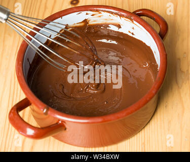 Pot with whisk and melted chocolate on wooden board Stock Photo