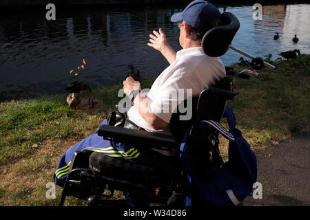 Image of a middle aged Wheelchair bound man feeding ducks by the grand union canal in Aylesbury, Buckinghamshire, England. Stock Photo