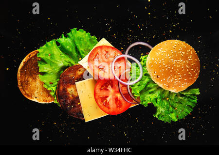 Flying ingredients for a homemade burger on a black background. Not diet food, unhealthy food. Stock Photo