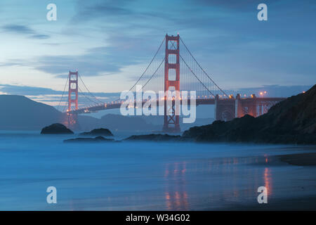 Classic panoramic view of famous Golden Gate Bridge seen from scenic Baker Beach in beautiful golden evening light on a sunset with blue sky and cloud Stock Photo