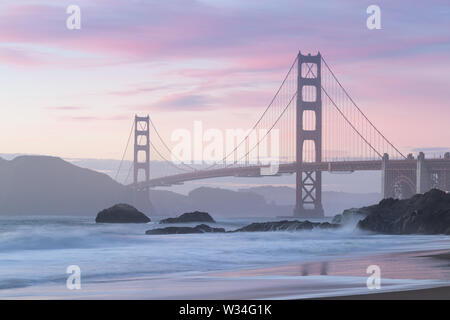 Classic panoramic view of famous Golden Gate Bridge seen from scenic Baker Beach in beautiful golden evening light on a sunset with blue sky and cloud Stock Photo