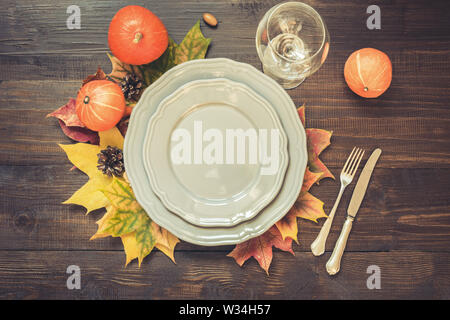 Autumn and Thanksgiving day table setting with fallen leaves, grey dish and silverware on wooden table. Top view. Stock Photo