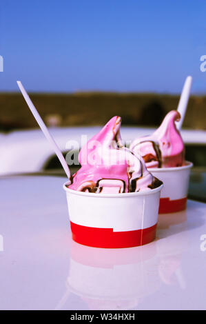 Two tubs of strawberry ice cream and fresh cream served on the roof of a car next to the beach Stock Photo