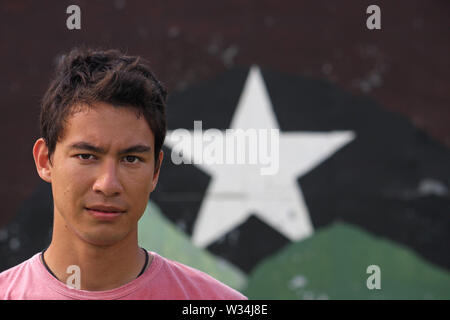Young Eurasian adult looking into the camera with a confident and serious look, while standing in front of a wall with a star on it. Stock Photo