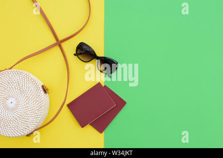 Beautiful round straw handbag and sunglasses with passports  on the yellow-green background. Trendy handbag. Stock Photo