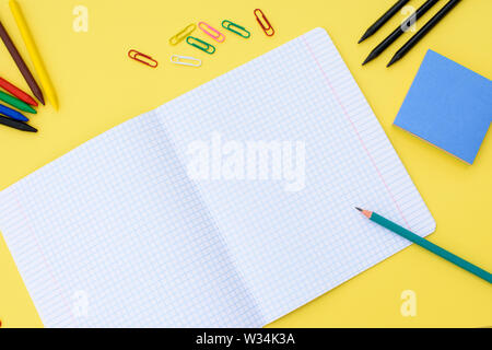 Notebook in a cage with a pencil, eraser, ruler, paper clips and other office supplies on a yellow background. Concept back to school. Place for text. Stock Photo
