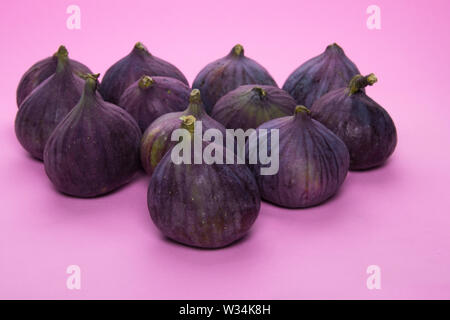 12 beautiful ripe purple figs are on a purple pink table. Several useful summer fruits on a bright pink background. Stock Photo
