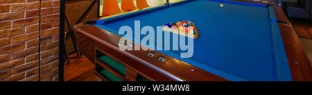 Retro blue pool table and billiard balls set up in restaurant with chairs and brick wall wide angle close up view Stock Photo