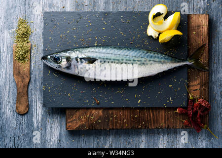 high angle view of a raw fresh mackerel on a slate tray placed on a rustic wooden table, next to some different spices Stock Photo