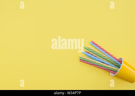Yellow paper cup with some striped tubes lies on a yellow background. Place for text. Stock Photo