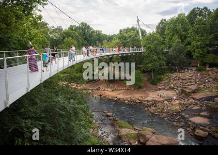 GREENVILLE, SC (USA) - July 5, 2019: Visitors to Falls Park linger on Liberty Bridge overlooking the Reedy River waterfalls. Stock Photo