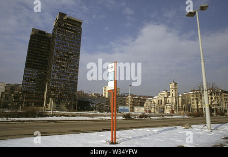 2nd April 1993 During the Siege of Sarajevo: the view across 'Sniper Alley' (Zmaja od Bosne) from the front of the Assembly Building. On the right is Saint Joseph’s Church (Roman Catholic); on the left, the twin Unis Towers. Behind the signpost in the centre is the Dr Abdulah Nakas General Hospital, known locally as the 'City' or 'French' Hospital during the war. Stock Photo