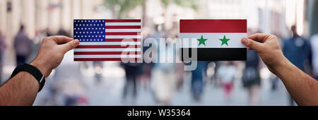 Two hands holding different flags, USA vs Syria on politics arena over crowded street background. Diplomacy future strategy, relations between countri
