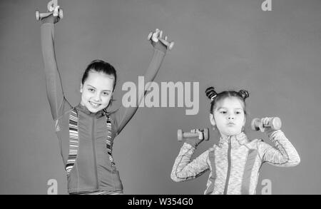 Toddler repeat exercise after sister. Sport exercises for kids. Healthy upbringing. Sporty babies. Following her sister. Girls cute kid exercising with dumbbells. Motivation and sport example concept. Stock Photo