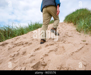 Senior man trudging up steep sand dune slope, Aberlady Nature Reserve, East Lothian, Scotland, UK Stock Photo