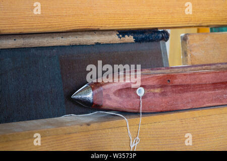 Weaving shuttle with metal cap and linen yarn ready for weaving on a wooden hand weaving loom Stock Photo