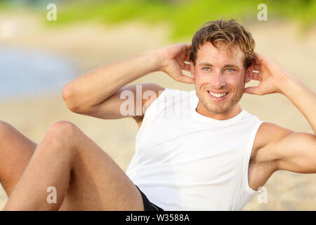 Fitness man doing crunches sit-ups on beach exercise outside. Fit male athlete exercising sit ups training on beautiful beach. Handsome sport model in cross training workout outdoors. Stock Photo
