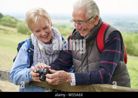 Senior Couple Hiking In Countryside Standing By Gate And Taking Photo With Camera Stock Photo