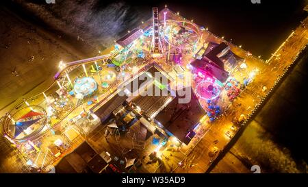 Aerial shot of a carnival at an attraction park near the beach at night Stock Photo