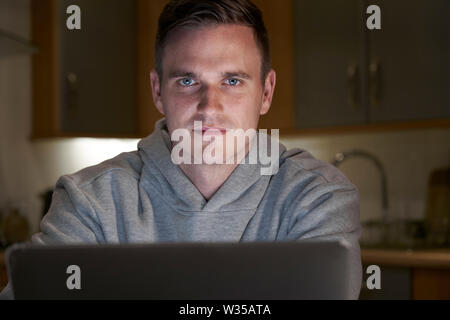 Portrait Of Suspicious Looking Man Using Laptop In Evening At Home Stock Photo