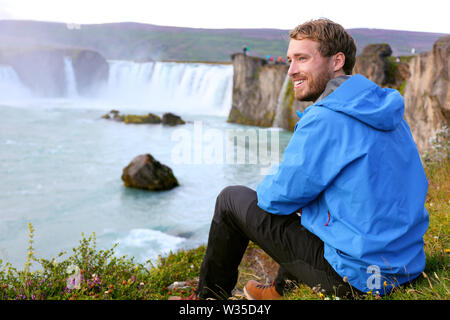 Iceland tourist relaxing by waterfall Godafoss. Man hiker resting on travel visiting tourist attractions and landmarks in Icelandic nature on Ring Road, Route 1. Stock Photo