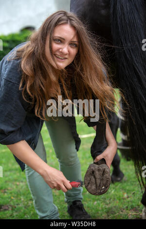 portrait of young brunette woman cleaning the hooves of her horse Stock Photo