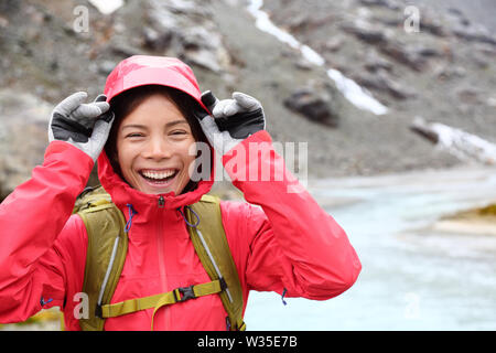 Laughing happy woman hiking with backpack in rain on trek living healthy active lifestyle. Smiling cheerful girl walking on hike in beautiful mountain nature landscape raining, Swiss alps, Switzerland Stock Photo