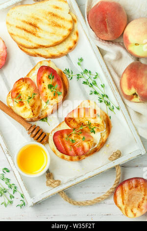 Gourmet summer Breakfast - sandwiches (bread toast, bruschetta) with grilled peaches, cream cheese (ricotta, mascarpone), thyme and honey on an old wh Stock Photo