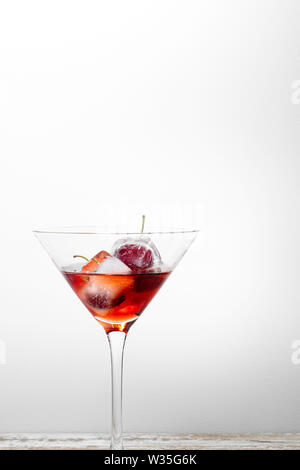 ice cubes with cherries inside into a red cocktail, white background textured with free space for text Stock Photo