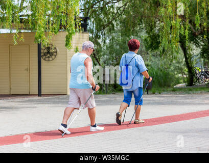 Senior couple walking with hiking sticks on treadmill along a lake in city park Stock Photo