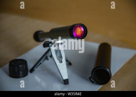 Spyglass on a small tabletop stand. Enlightenment lens beautifully shimmers colors. Black plastic case with open lid. Selective focus close up. Stock Photo