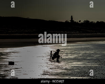 silhouette of a man sitting in a camping chair and is fishing in an dramatic backlight Stock Photo