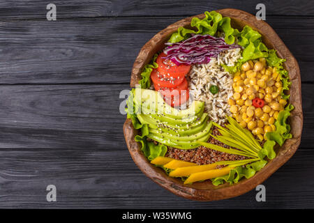 Buddha bowl with chickpea, avocado, wild rice, quinoa seeds, bell pepper, tomatoes, greens, cabbage, lettuce on black wooden table. Top view with copy Stock Photo