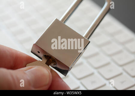 Fingers turning a key on stainless padlock in front of computer keyboard. PC network security, data security and antivirus protection concept. - Image Stock Photo