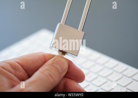 Fingers turning a key on stainless padlock in front of computer keyboard. PC network security, data security and antivirus protection concept. - Image Stock Photo